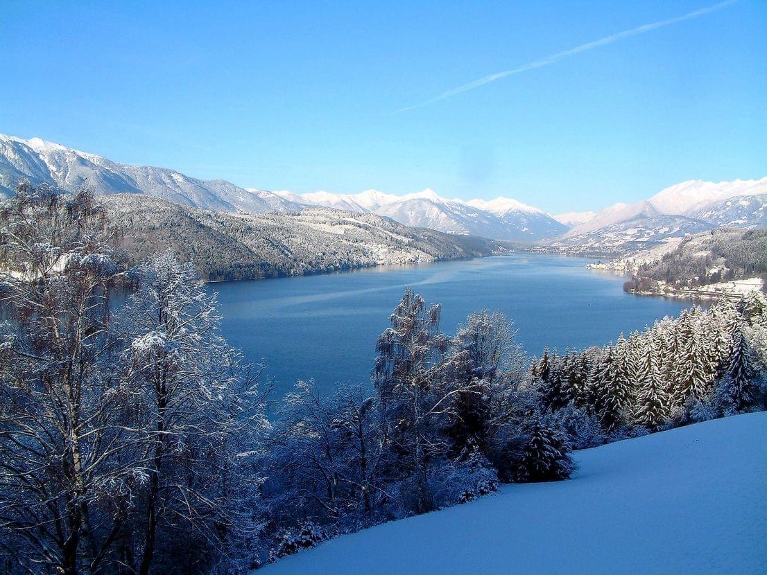 Schneebedeckter Millstätter See mit Bergen und Tannenwäldern unter klarem blauen Himmel